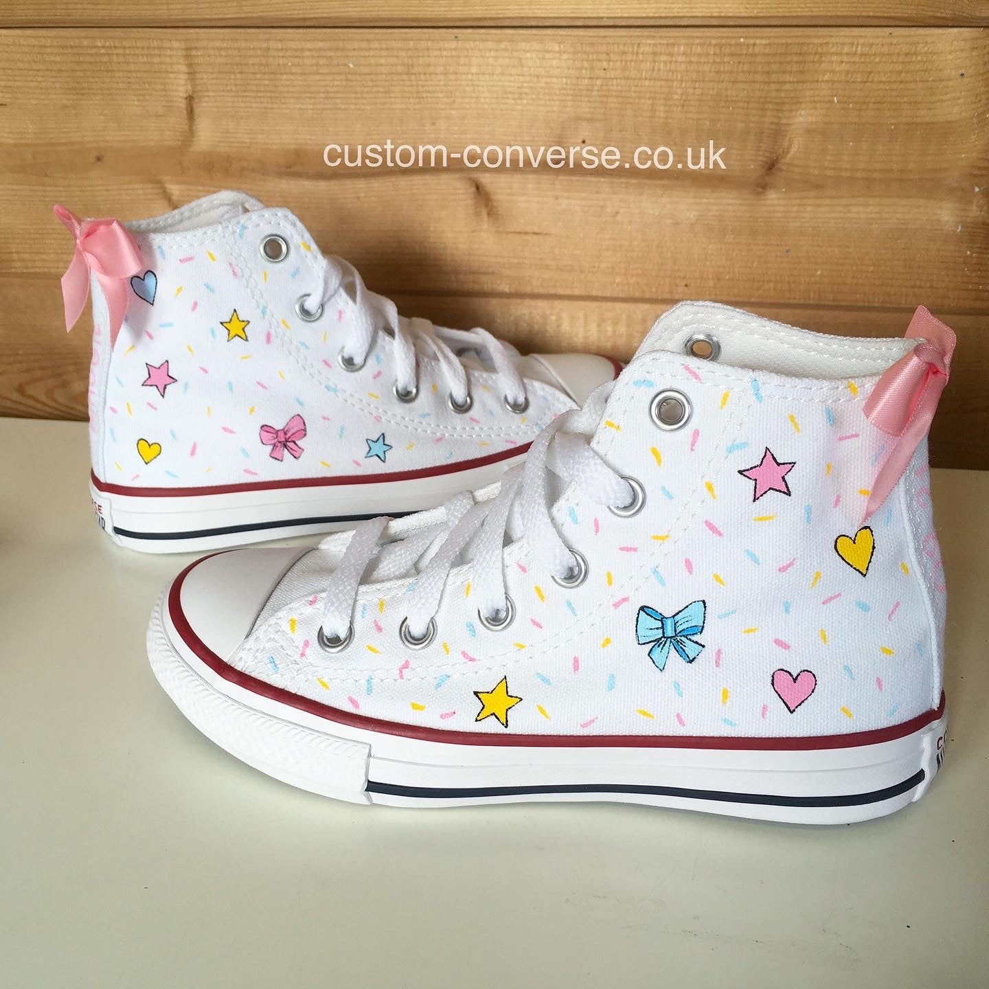 Kids custom trainers hand-painted with a design of bows, stars and confetti in pastel pink yellow and blue colours