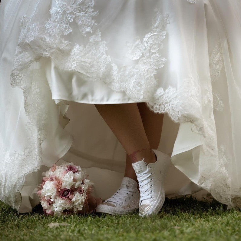 Image of a Bride wearing a pair of custom wedding trainers under her wedding dress with bouquet placed next to her feet